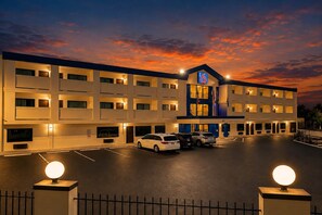 A multi-story hotel with a parking lot, a prominent '6' sign, and a sunset sky. - 2 Full Beds|Non-Smoking,Micfridge (Atlanta)