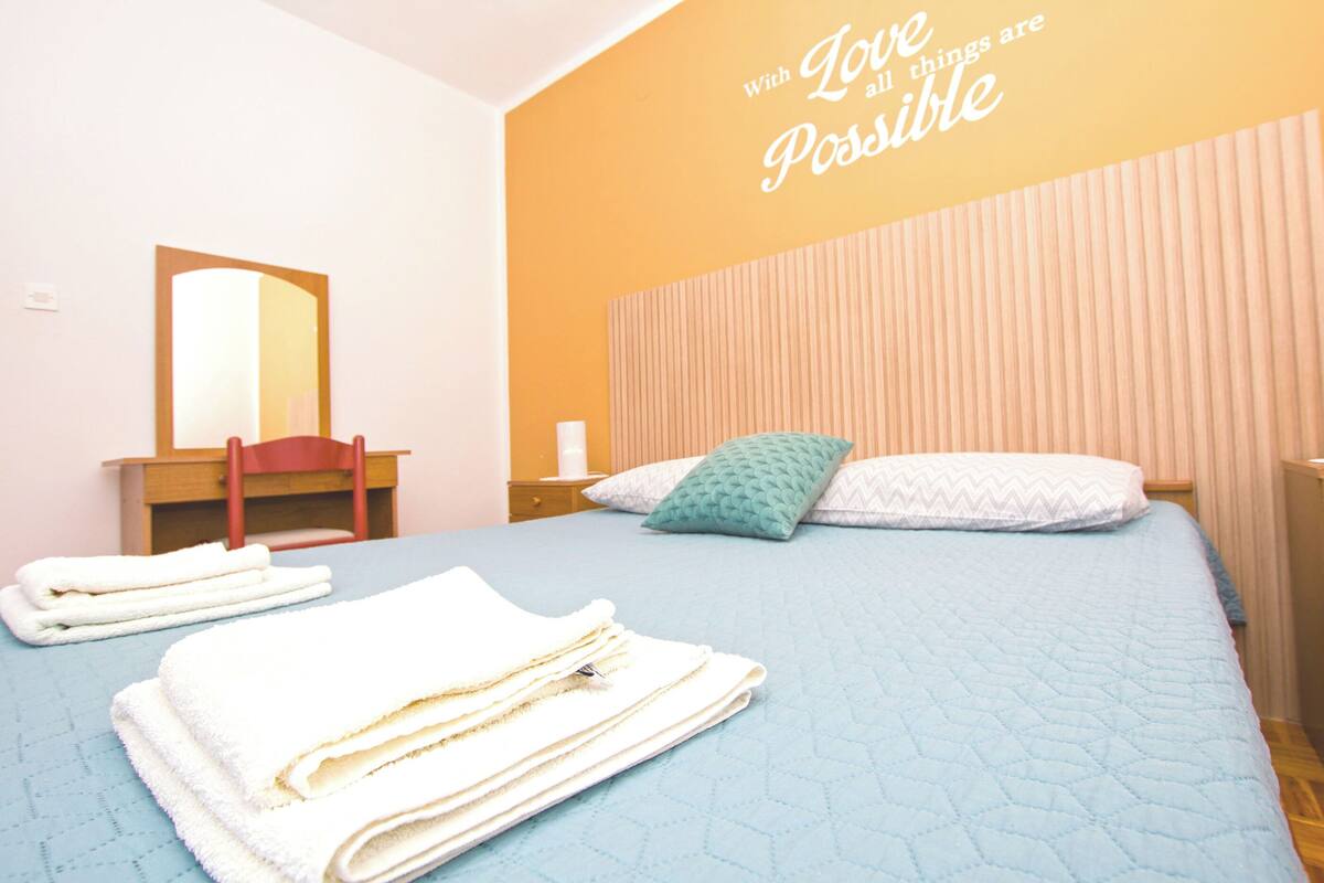 A bedroom with a bed, a chair, a mirror, and a wall with a motivational quote.