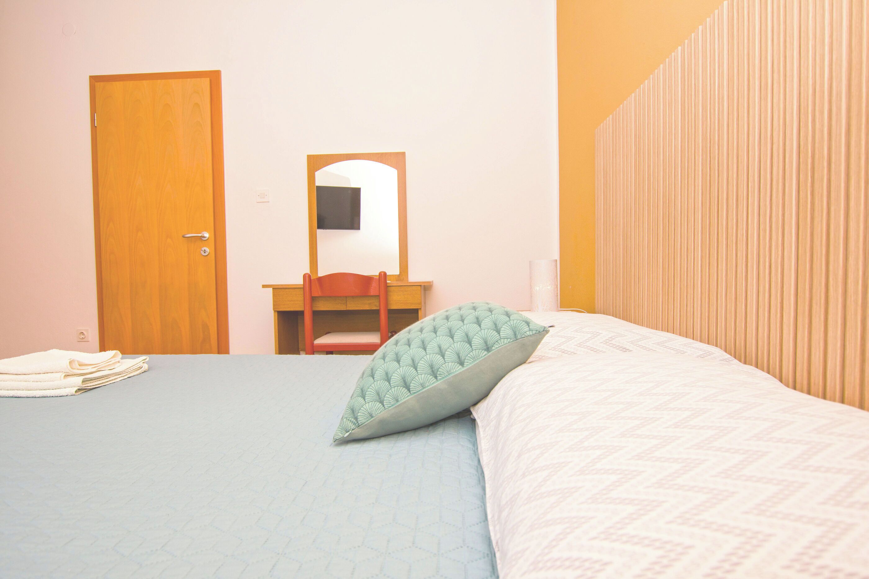 A bedroom with a bed, a chair, a mirror, and a door.