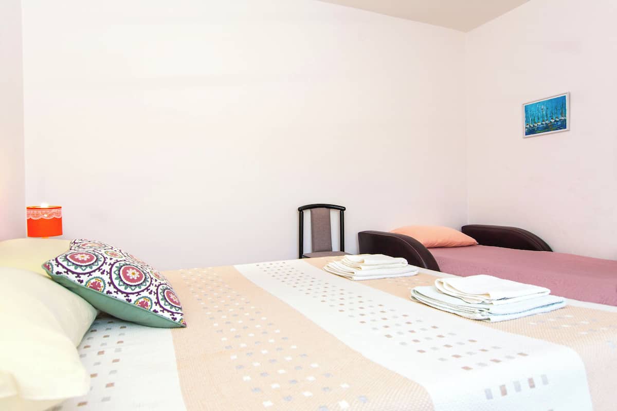 A hotel room with a bed, a chair, a table with towels, a lamp, and a painting on the wall.