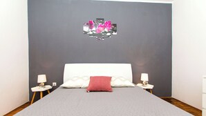 Una camera da letto con un letto grande, due comodini con lampade, un cuscino rosso e un quadro appeso al muro.