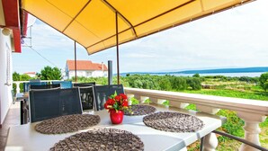 Una terrazza con tavolo apparecchiato per mangiare, una tenda gialla e vista sul mare e sul verde.