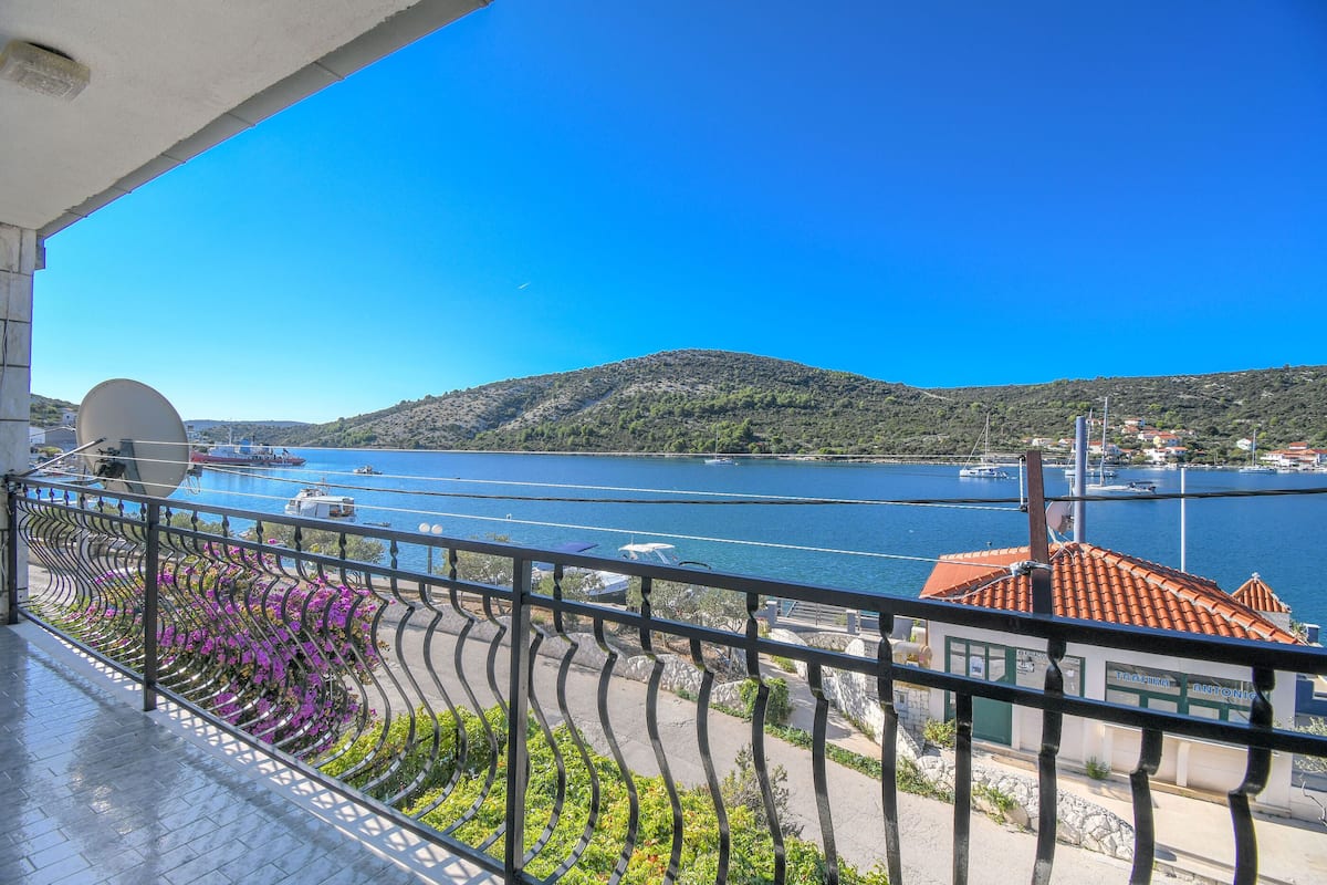Un balcon avec vue sur une étendue d’eau, une montagne et un bâtiment doté d’un toit rouge.