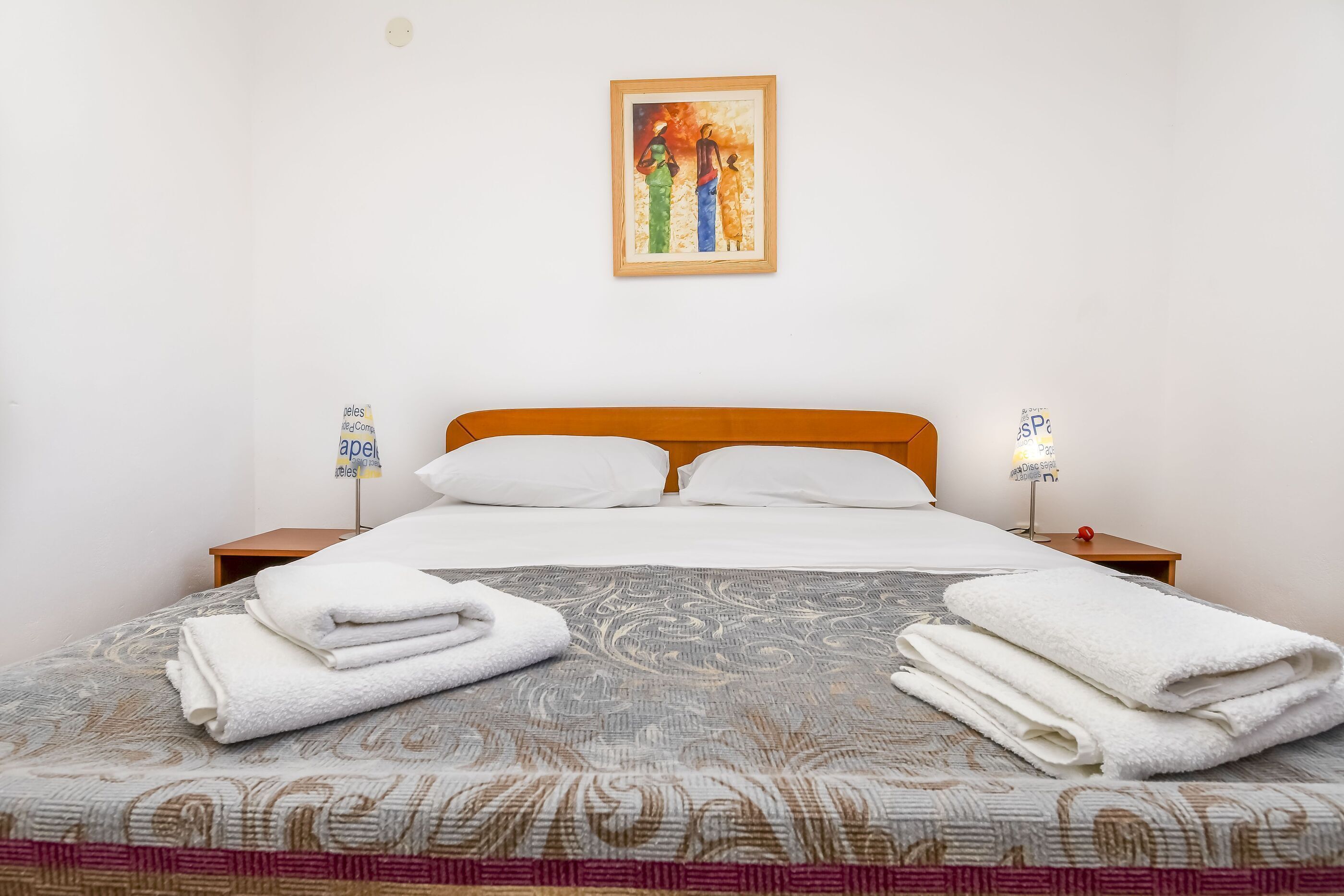 Ein ordentlich bezogenes Bett mit weißen Handtüchern, einem hölzernen Kopfteil und einem gerahmten Gemälde an der Wand.
