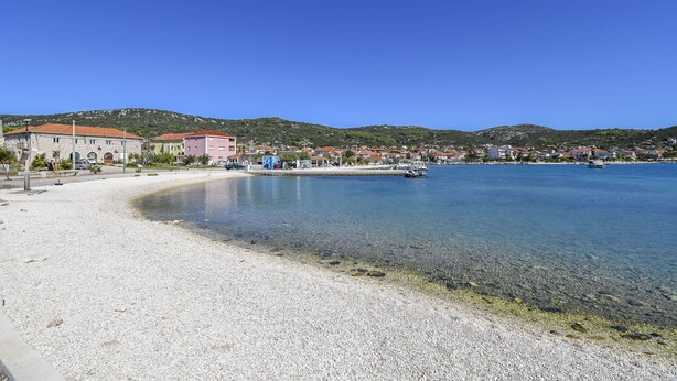Eine Küstenstadt mit Kiesstrand, klarem Wasser und Gebäuden entlang der Uferlinie.