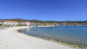 A coastal town with a pebble beach, clear waters, and buildings along the shore.