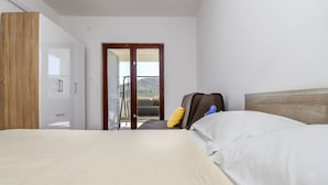 Ein Hotelzimmer mit Bett, Schrank, Koffer und einem Balkon mit Blick.