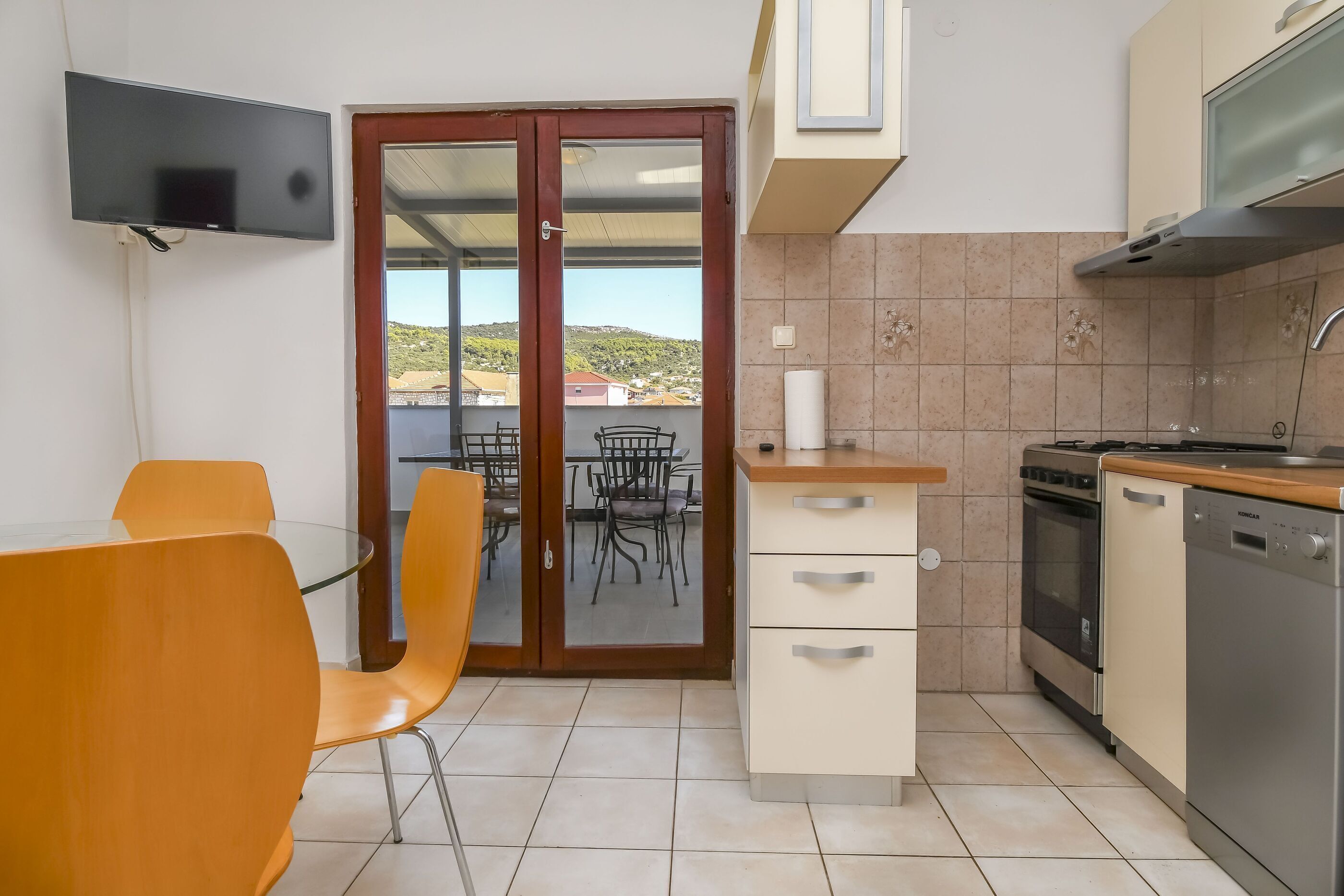 A compact kitchen with a dining area, a TV mounted on the wall, and a view of the outside.