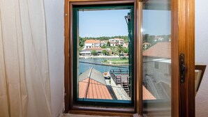 A view through a window of a building with a wooden frame, a balcony, and a river with boats. - Apartments Draga (Jelsa)