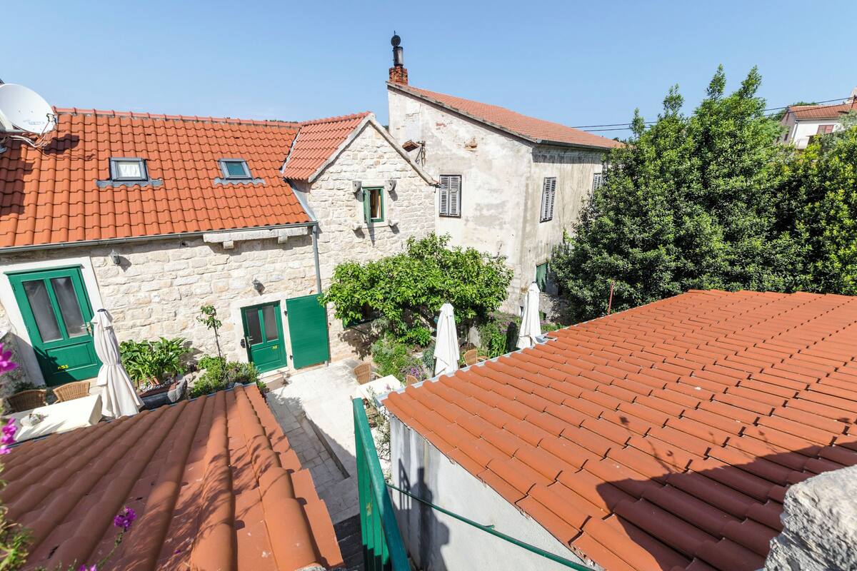 Un bâtiment traditionnel en pierre, avec un toit recouvert de tuiles rouges, des volets verts et un petit balcon.