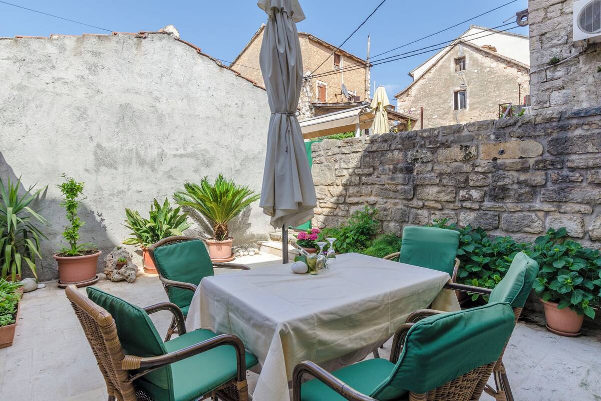 Une terrasse avec une table et des chaises, entourée de plantes en pot et d’un mur de pierre.