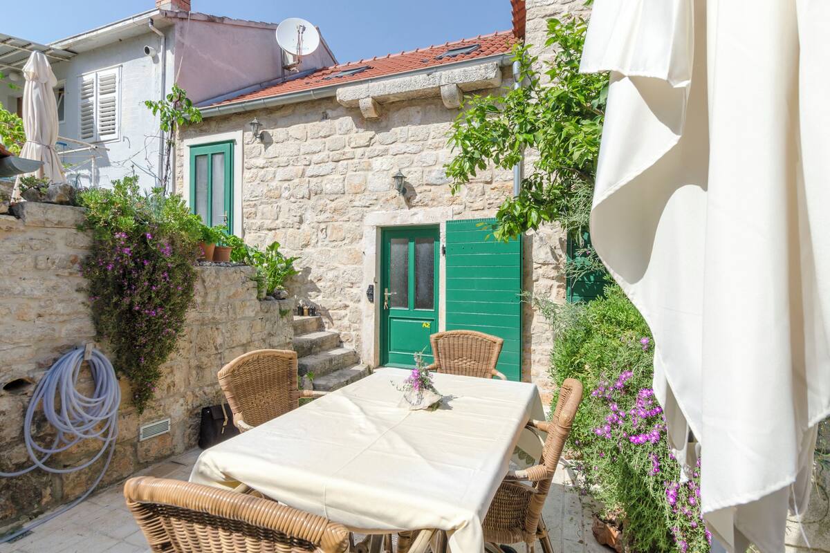 Un bâtiment en pierre avec une porte verte, une table entourée de chaises et des plantes en pot.