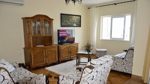 Ein Wohnzimmer mit einem Holzkabinett, einem Fernseher, gemusterten Sofas und einem Fenster.