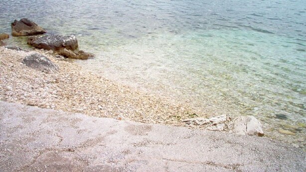 Un lago transparente con orilla pedregosa y rocas visibles.