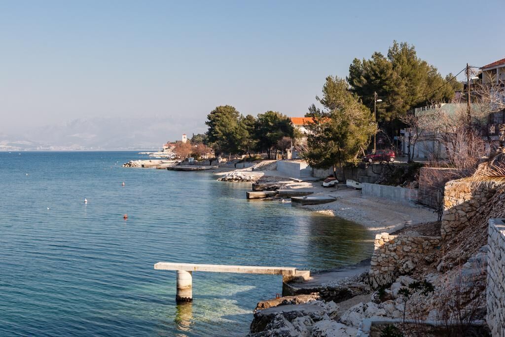 A coastal area with a clear view of the sea, a stone wall, and some buildings in the background.