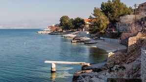 A coastal area with a clear view of the sea, a stone wall, and some buildings in the background. - Apartments Anda (Trogir)