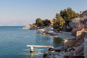 A coastal area with a clear view of the sea, a stone wall, and some buildings in the background. - Apartments Anda (Trogir)