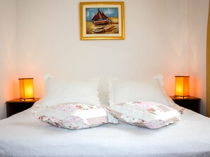 Una cama con almohadas florales, dos lámparas de noche y un cuadro enmarcado de un velero en la pared.