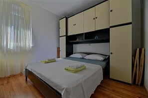 A bedroom with a bed, a wardrobe, and a window with sheer curtains. - Apartments Nela (Postira)