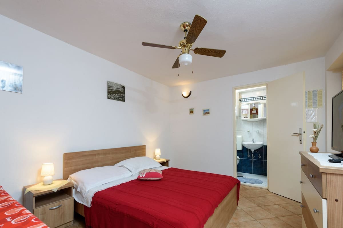 Een slaapkamer met een bed, nachtkastjes, een plafondventilator en een zichtbare badkamer door een open deur.