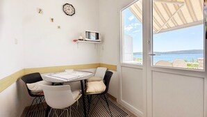 Une chambre d’angle avec une table et des chaises, un four à micro-ondes posé sur une étagère, une horloge et une vue sur la mer par une grande fenêtre.