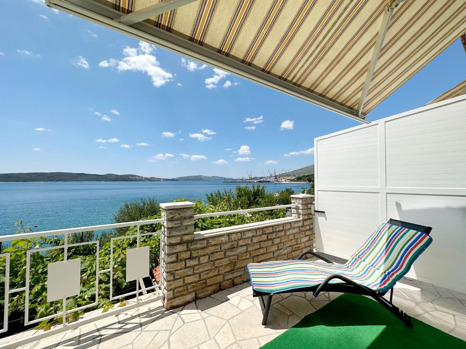 Un balcon donnant sur une étendue d’eau, une chaise à rayures et un mur blanc.