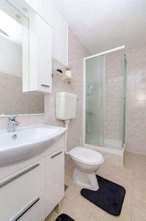 A bathroom with a white sink, toilet, and glass-enclosed shower. - Apartment Tonka (Jelsa)