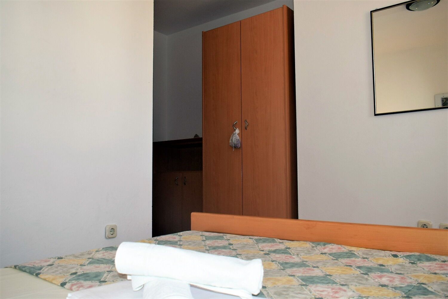 A bedroom with a bed, a wooden wardrobe, and a mirror on the wall.