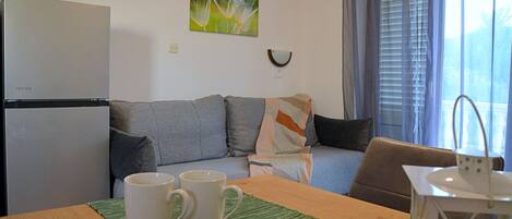 Un salon avec un canapé, une table basse sur laquelle sont posées des tasses, un réfrigérateur et une fenêtre avec des rideaux.