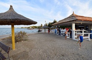 Een restaurant aan het strand met terras, rieten dak en uitzicht op zee.