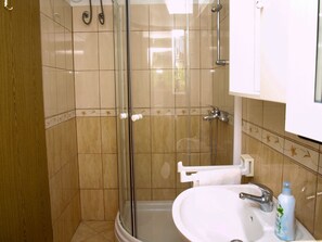 Un baño con ducha de vidrio, un lavamanos blanco y una botella de champú.