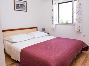 Un dormitorio con cama, mesita de noche, ventana con cortinas y un cuadro en la pared.