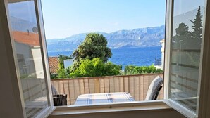 Ein Zimmer mit einem Bett, einem Fenster mit Blick auf das Meer und die Berge sowie einem kleinen Tisch.