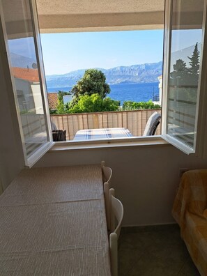 Una habitación con cama, ventana con vista al mar y las montañas, y una mesita.