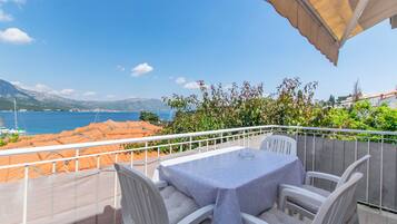 A balcony with a table and chairs, overlooking a coastal area with mountains and a body of water.