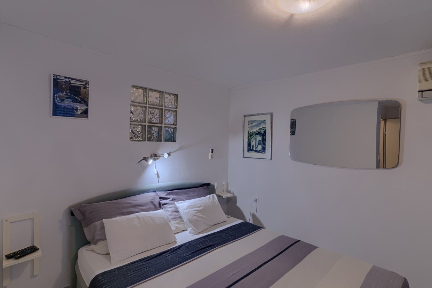 A bedroom with a bed, a bedside table, a lamp, and wall art.