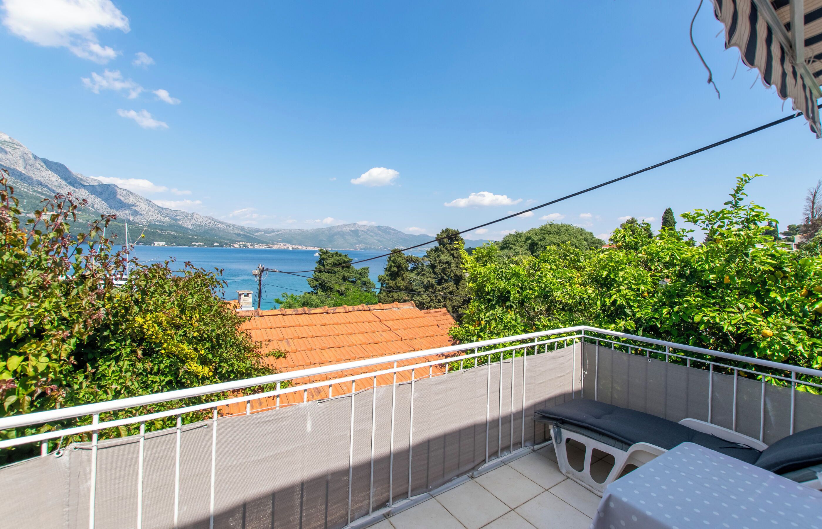 A balcony with a view of the sea, a table, and a chair.