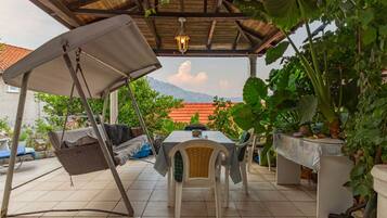 An outdoor patio with a swing chair, a table with chairs, and potted plants.