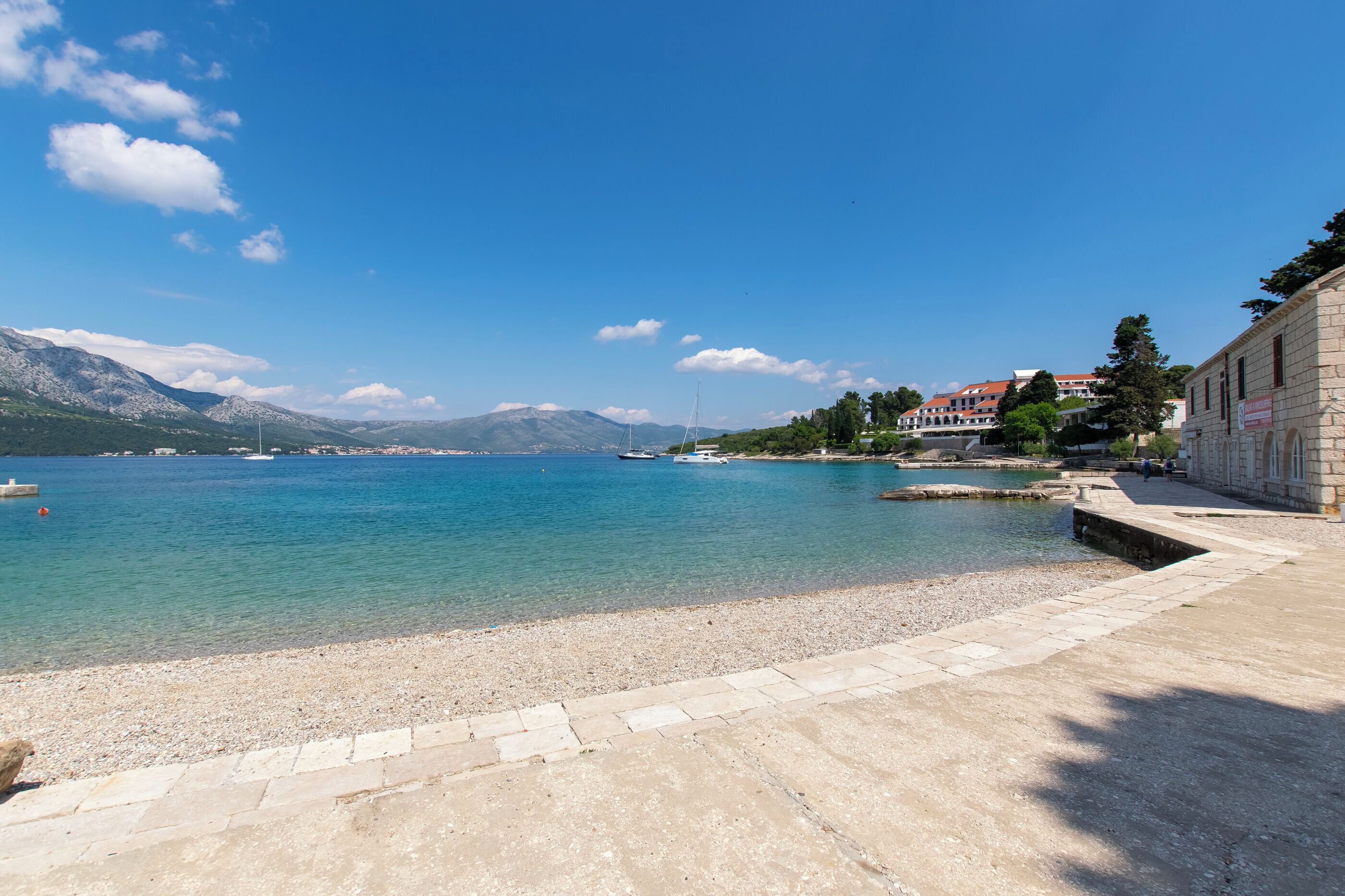 A coastal area with a clear blue sky, calm sea, and a stone building with a red roof.