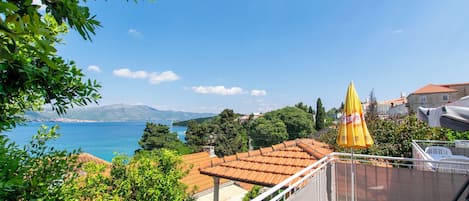 A balcony with a view of the sea, a yellow umbrella, and a white chair.