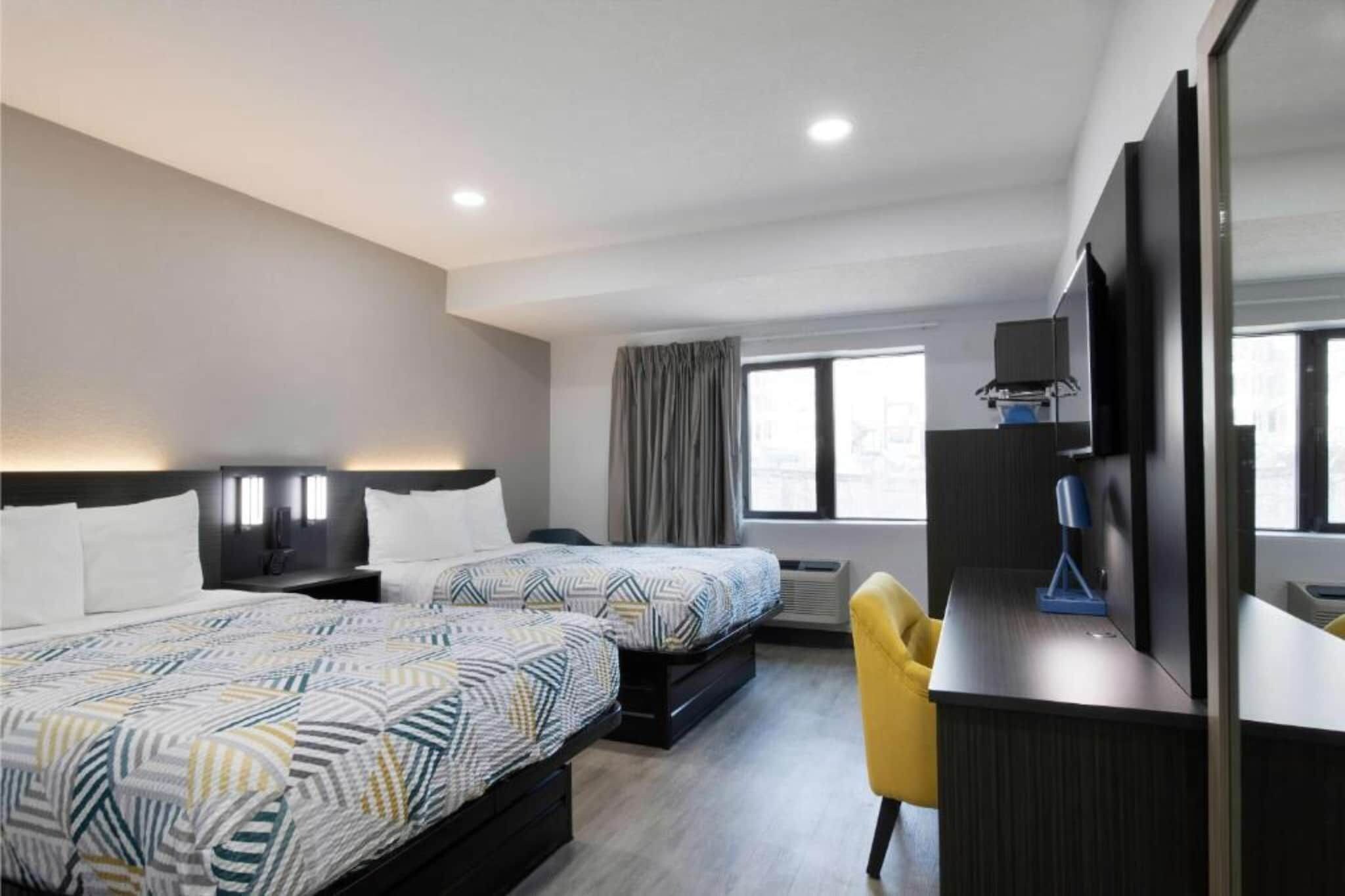 A hotel room with two beds, a desk, a chair, a TV, and a window.