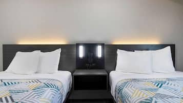 A hotel room with two beds, each with white bedding and a patterned duvet. There are two bedside tables with lamps and a wall-mounted light fixture between the beds.