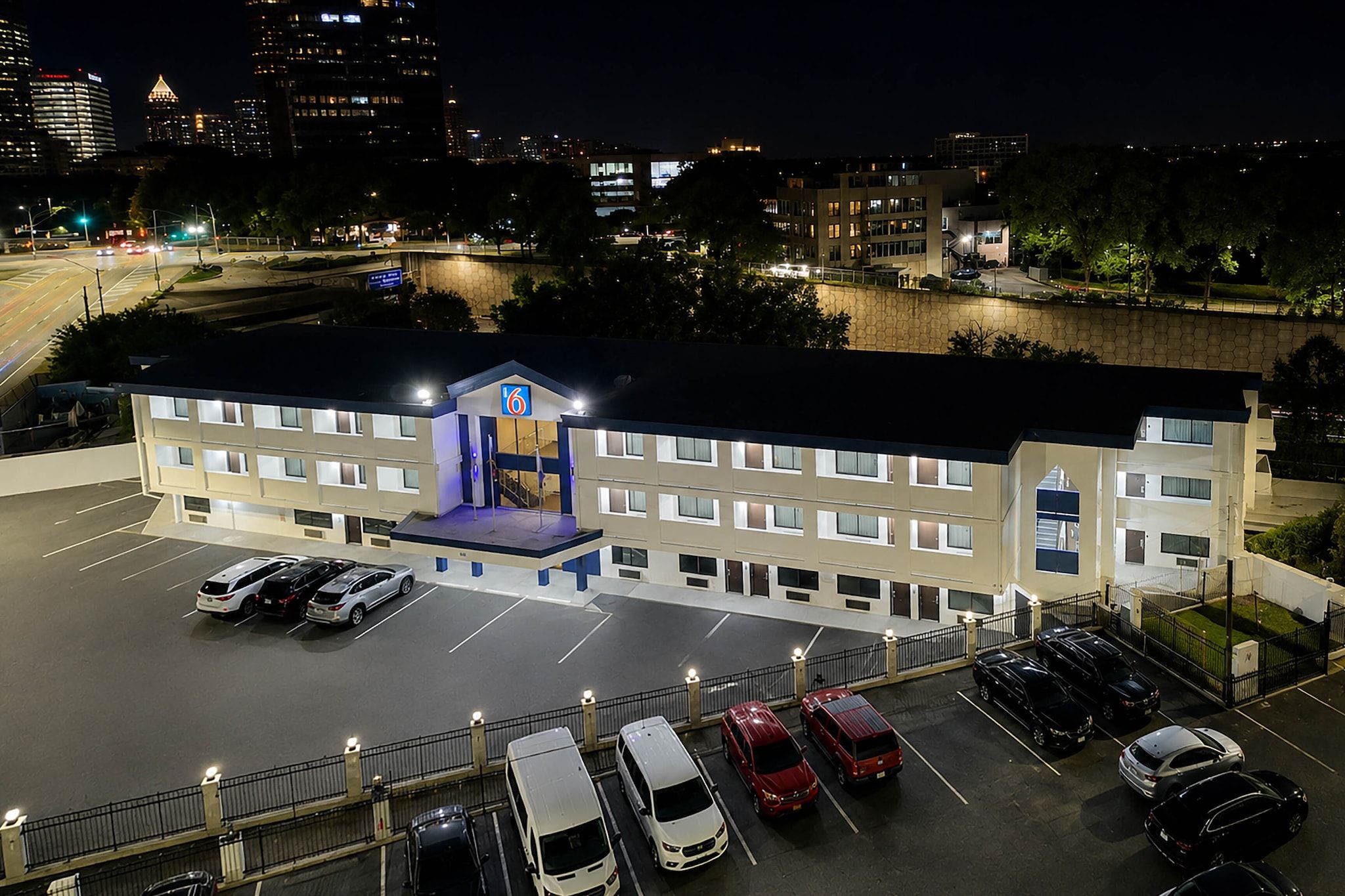 A multi-story hotel with a parking lot and a view of the city skyline at night.