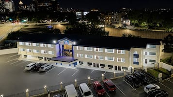 A multi-story hotel with a parking lot and a view of the city skyline at night.