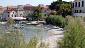 A waterfront area with boats docked, stone buildings with red roofs, and a sandy beach. - Apartments Brane (Postira)