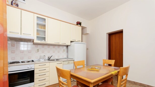 A compact kitchen with a dining area, including a stove, oven, refrigerator, and a table with chairs. - Apartments Brane (Postira)