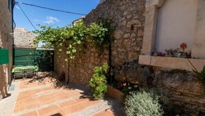 A stone-walled courtyard with a tiled floor, a table with chairs, and a shelf with potted plants. - Apartments Brane (Postira)