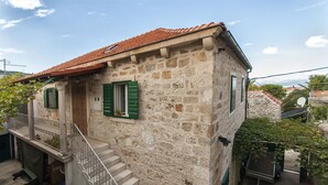A stone house with a red-tiled roof, green shutters, and a small balcony. - Apartments Brane (Postira)