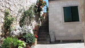 A narrow stone pathway leading to a building with a window and a door. - Apartments Brane (Postira)