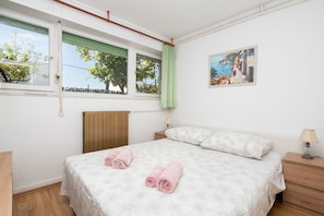Une chambre à coucher avec un lit, deux tables de chevet, une fenêtre donnant sur un beau paysage et un tableau accroché au mur.